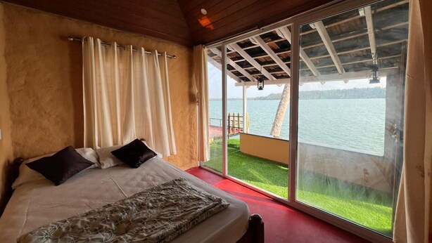 A bedroom with a bed, curtains, and a view of a body of water through large sliding doors. - Native Retreats Varkala (Hariharapuram)
