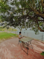 Una persona sentada a una mesa bajo un árbol junto al agua.