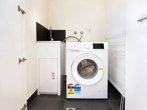 A compact laundry room with a front-loading washing machine, a small cabinet, and a water heater. - Heart of Doncaster 1BR Apt with  Wi-FI Parking (Doncaster)