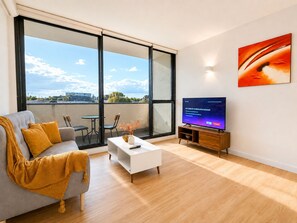 A modern living room with a sofa, coffee table, and TV, large windows with a city view, and a painting on the wall. - Heart of Doncaster 1BR Apt with  Wi-FI Parking (Doncaster)