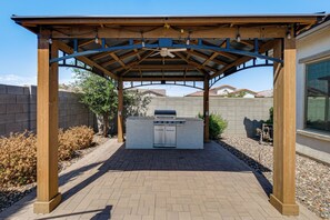 Ein Außenbereich mit Grillplatz, einer Pergola und einem gepflasterten Weg.