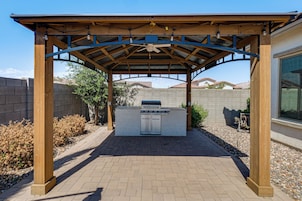 Un área de barbacoa al aire libre con un pérgola arriba, una parrilla empotrada y un camino de ladrillo.