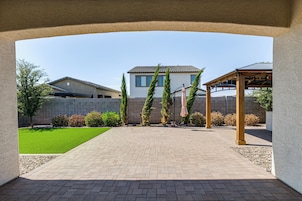 A courtyard with a paved walkway, a pergola, and a house in the background.