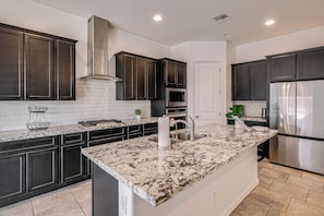 A modern kitchen with dark cabinetry, a stainless steel refrigerator, and a marble countertop. - Wfh-friendly Queen Creek Retreat w/ Pool Access (Queen Creek)