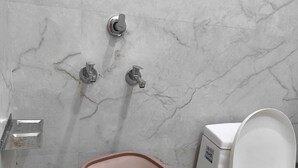 A bathroom with a marble wall, a white toilet, and a pink bucket. - COMFORT HOME STAY (Agra)