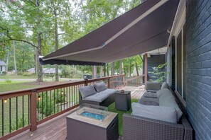 Um deck coberto ao ar livre com móveis de vime, uma mesa com tampo de vidro e vista para uma área residencial.