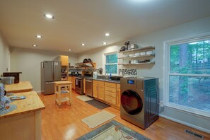 A modern kitchen with stainless steel appliances, wooden cabinets, and a large window offering a view of the outdoors. - Fire Pit & Grill! Wooded Durham Retreat (Durham)