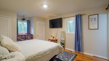 Quarto com cama, cômoda, televisão e janela com cortinas.