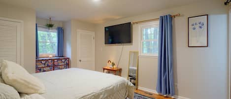 Un dormitorio con cama, cómoda, televisor y ventana con cortinas.