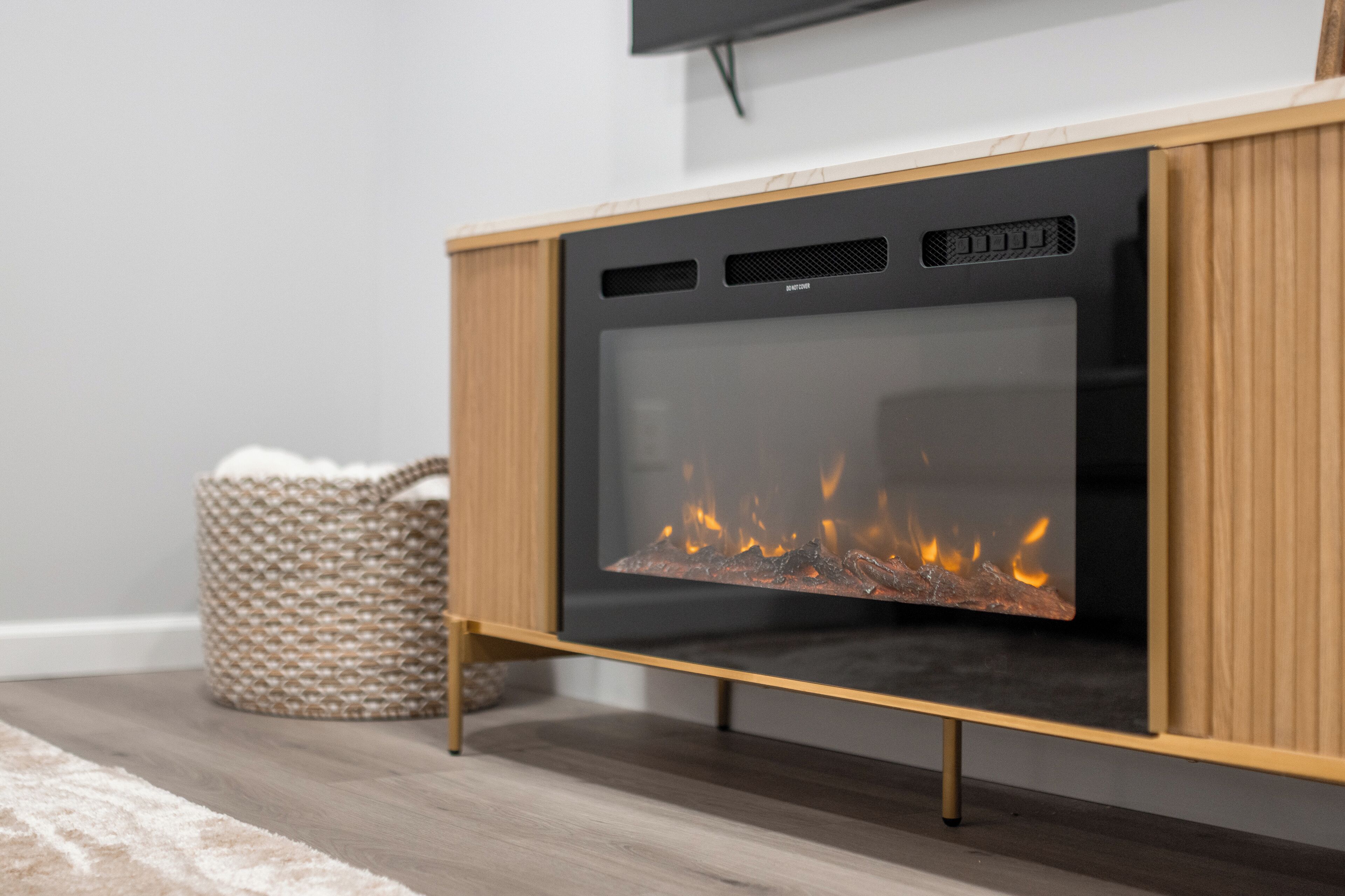 Ein moderner Kamin mit Glasscheibe, einem Holzschrank und einem gewebten Korb daneben.