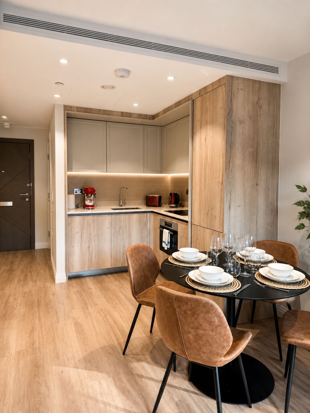 A modern kitchen with built-in appliances, a dining area with a round table set for four, and a wooden accent wall.
