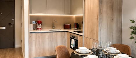 A modern kitchen with built-in appliances, a dining area with a round table set for four, and a wooden accent wall.