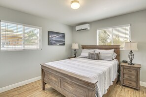 Ein Schlafzimmer mit einem hölzernen Bett, zwei Nachttischen mit Lampen, einem zusätzlichen Tischchen und einer Wand-Klimaanlage.