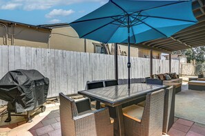 Eine Terrasse im Freien mit Tisch, Stühlen, einem Grill und einem großen Sonnenschirm.