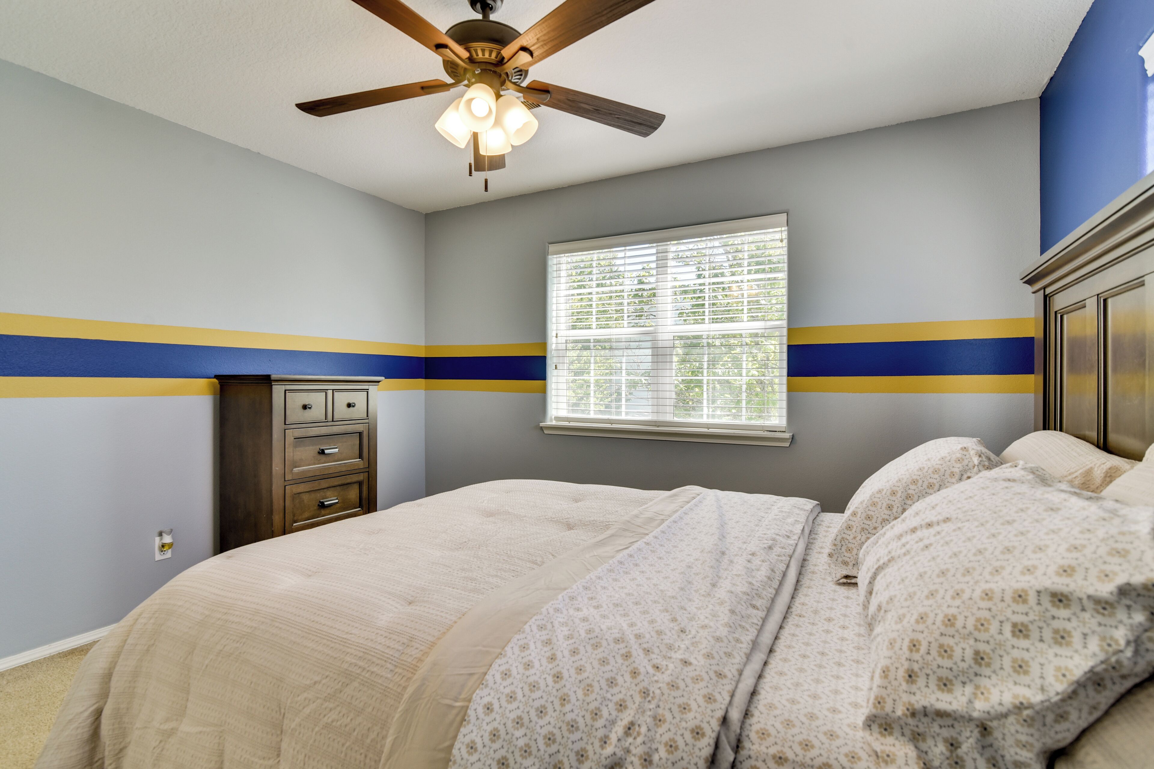 A bedroom with a bed, a ceiling fan, a window with blinds, and a dresser.