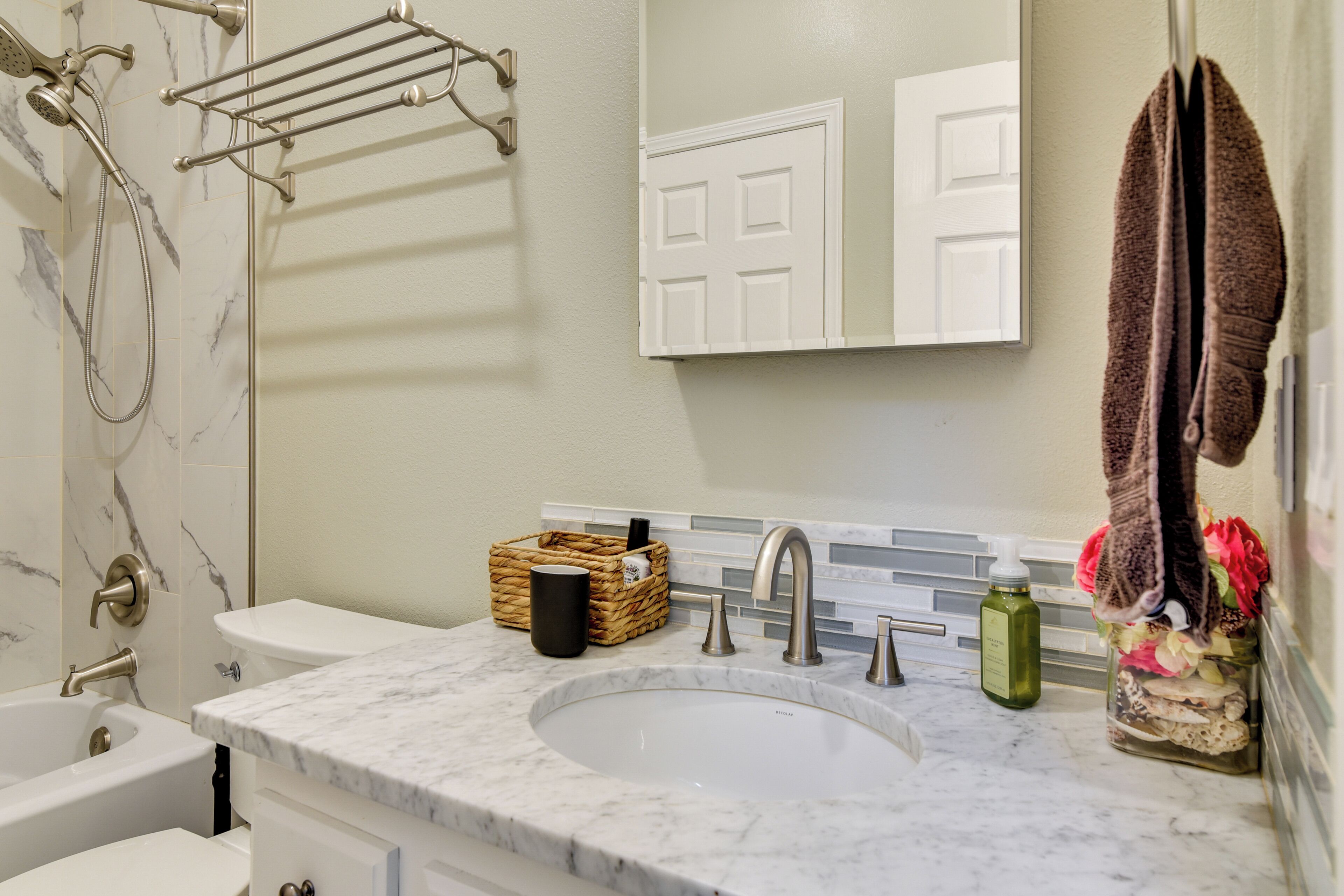 A bathroom with a bathtub, a sink, a mirror, and a towel rack.