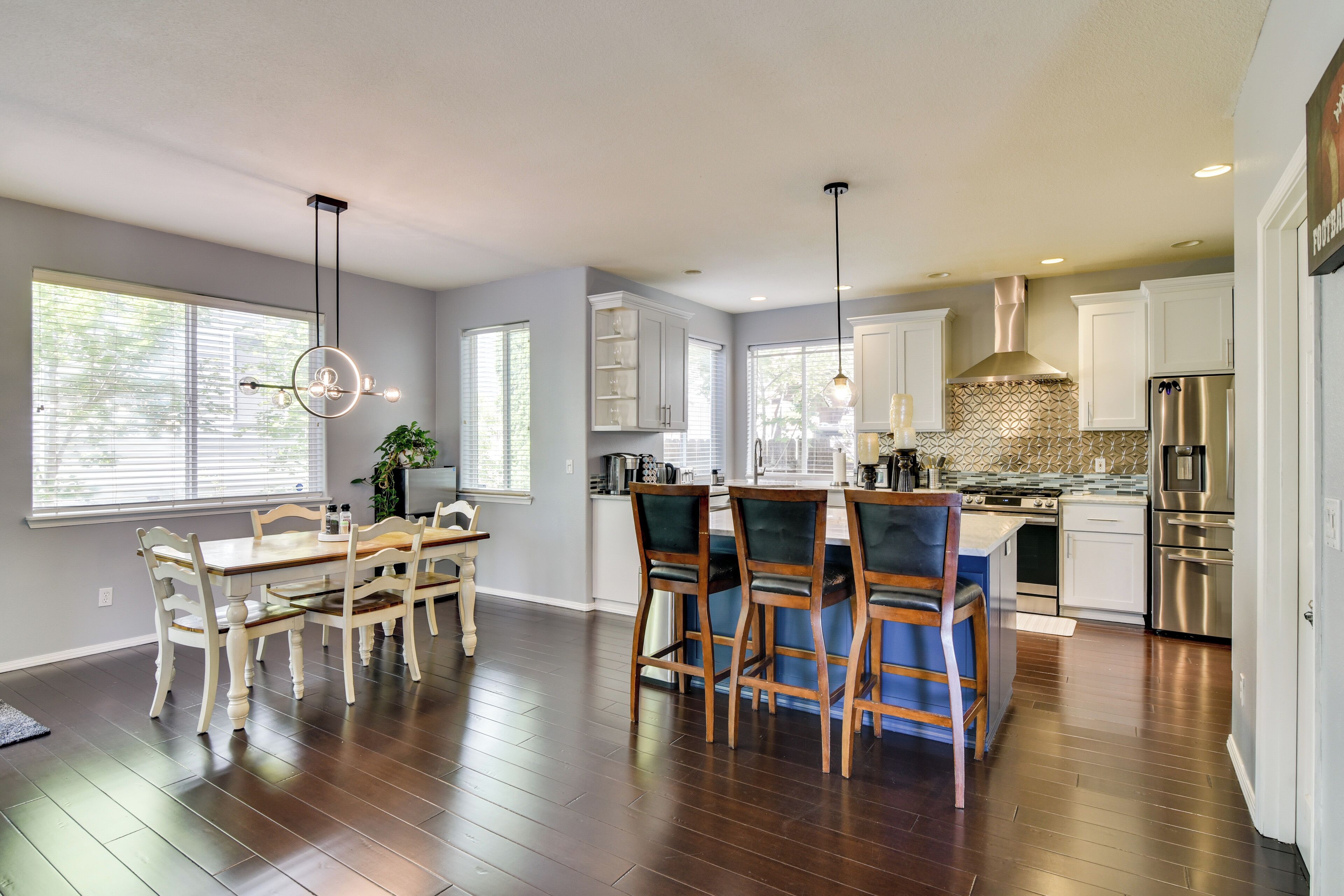 A modern kitchen with wooden flooring, white cabinetry, and stainless steel appliances.