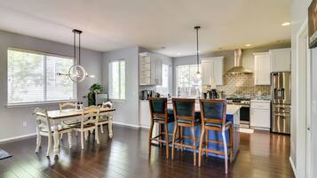 A modern kitchen with wooden flooring, white cabinetry, and stainless steel appliances.