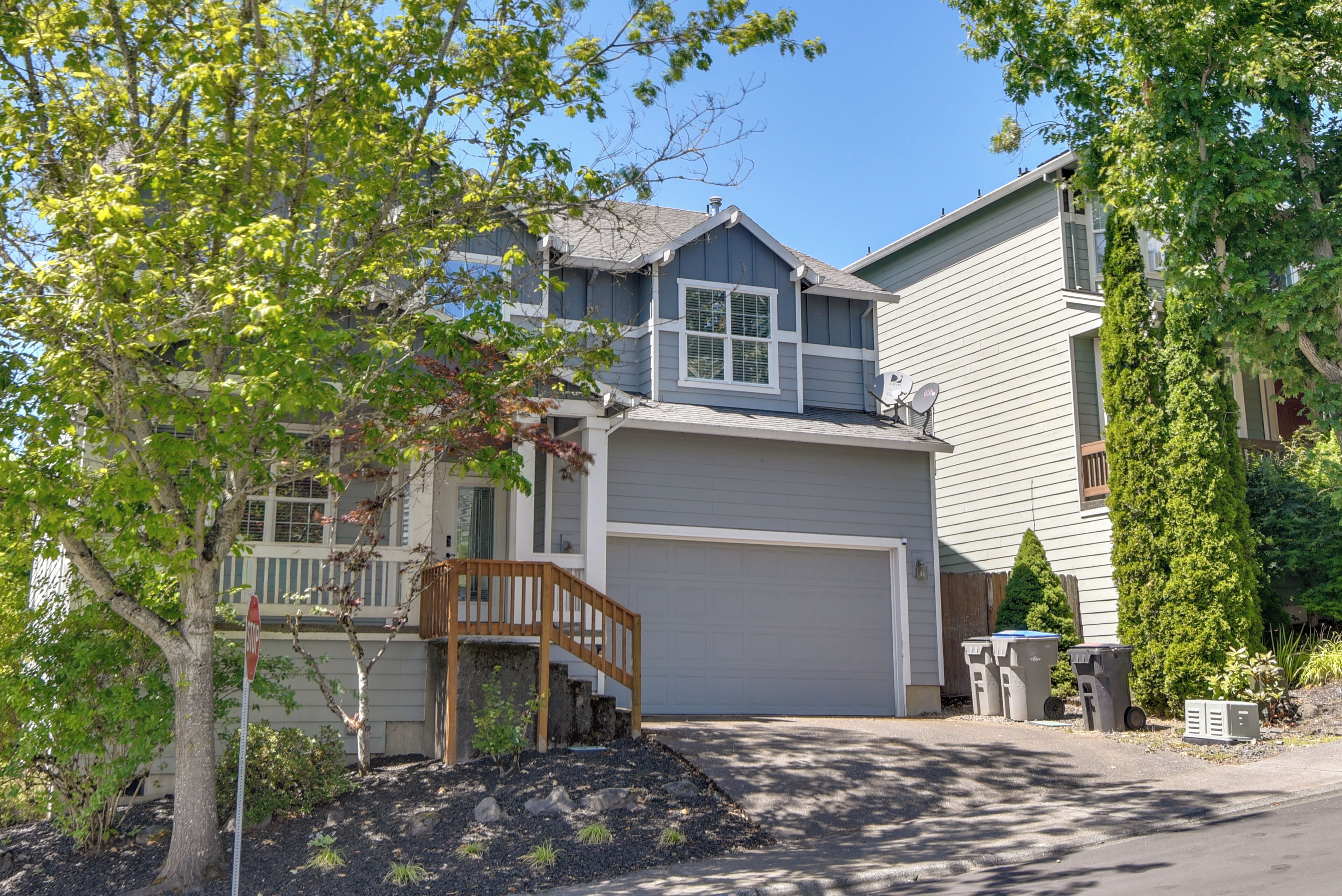 A two-story residential house with a front garage, a wooden staircase leading to the entrance, and a landscaped front yard.