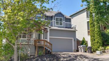 A two-story residential house with a front garage, a wooden staircase leading to the entrance, and a landscaped front yard.