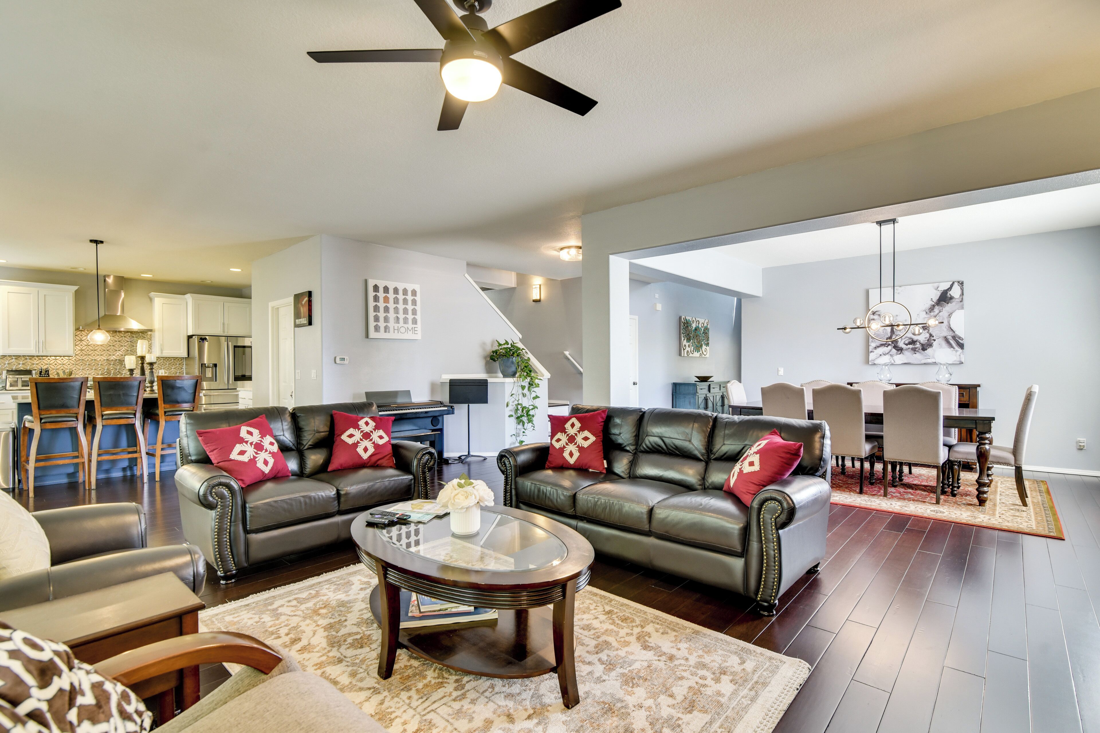 A spacious living room with a ceiling fan, a dining area with a table and chairs, and a kitchen in the background.