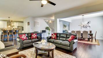 A spacious living room with a ceiling fan, a dining area with a table and chairs, and a kitchen in the background.