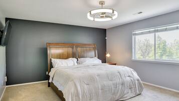 A bedroom with a bed, a nightstand, a lamp, a window with a view of trees, and a ceiling light fixture.