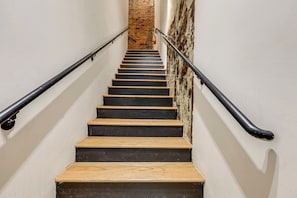 Eine Treppe mit Holzdielen und schwarzen Wangen, gesäumt von Metallgeländern, die zu einer Ziegelwand führt.