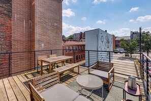 Eine Dachterrasse mit einem Holztisch und Stühlen, einem runden Tisch mit Metallgestell und Blick auf die Stadtlandschaft.