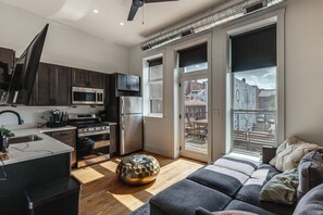 Uma cozinha moderna com eletrodomésticos de aço inoxidável, uma área de refeições com sofá e vista para a paisagem urbana.