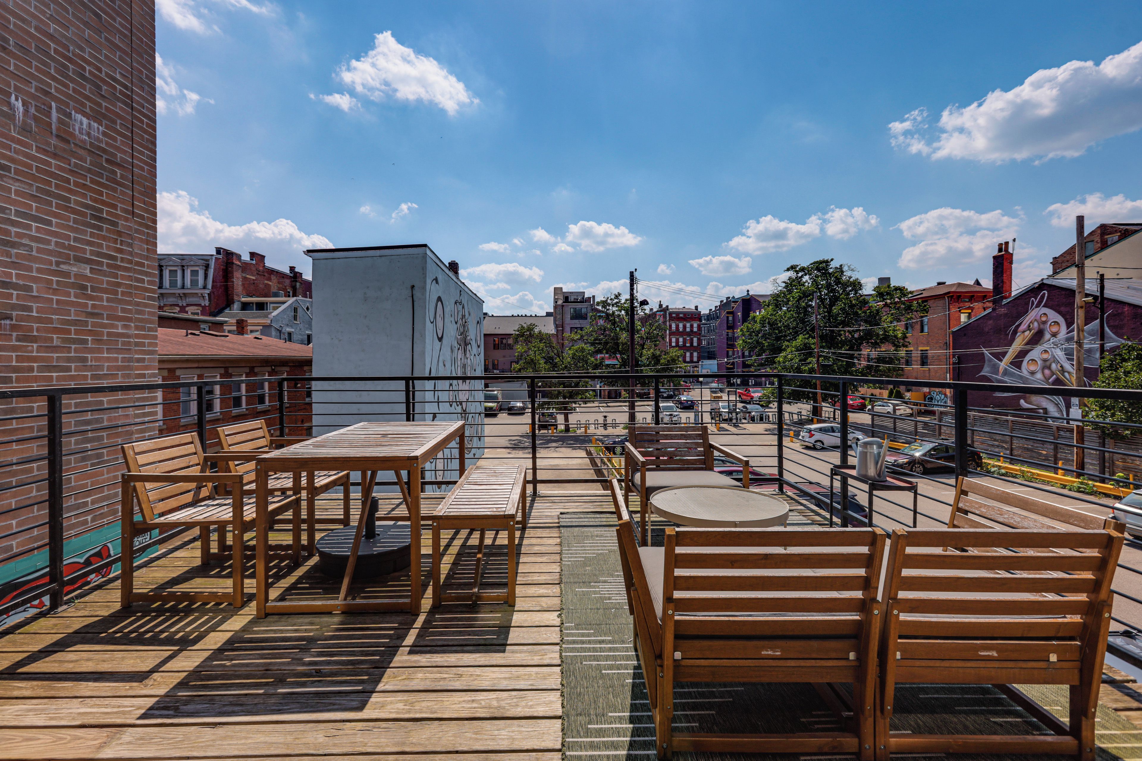 Una terraza en la azotea con mobiliario de madera, vistas de la ciudad y cielo despejado.
