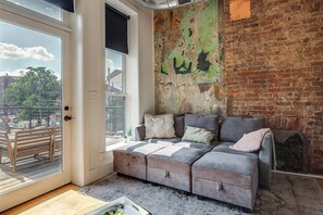 Ein modernes Wohnzimmer mit einem grauen Sofa, einer Backsteinwand und einem großen Fenster.