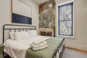 A bedroom with a bed, a window, a brick wall, and a painting. - Walk to Findlay Market! Over-the-rhine Condo (Cincinnati)