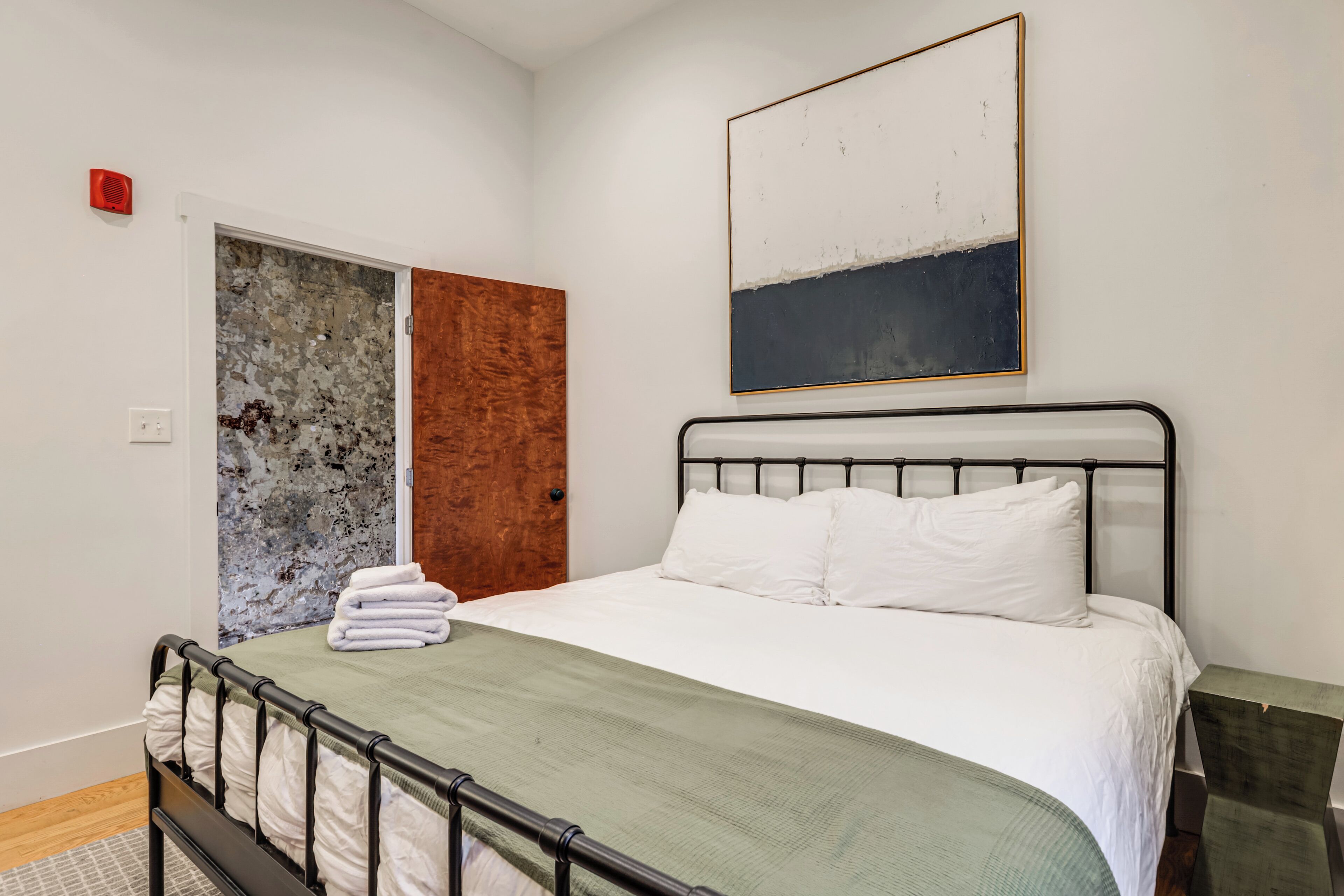 Um quarto com uma cama, uma porta e um quadro na parede.