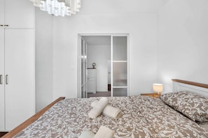A bedroom with a bed, a nightstand, a lamp, a wardrobe, and a sliding door leading to a bathroom.