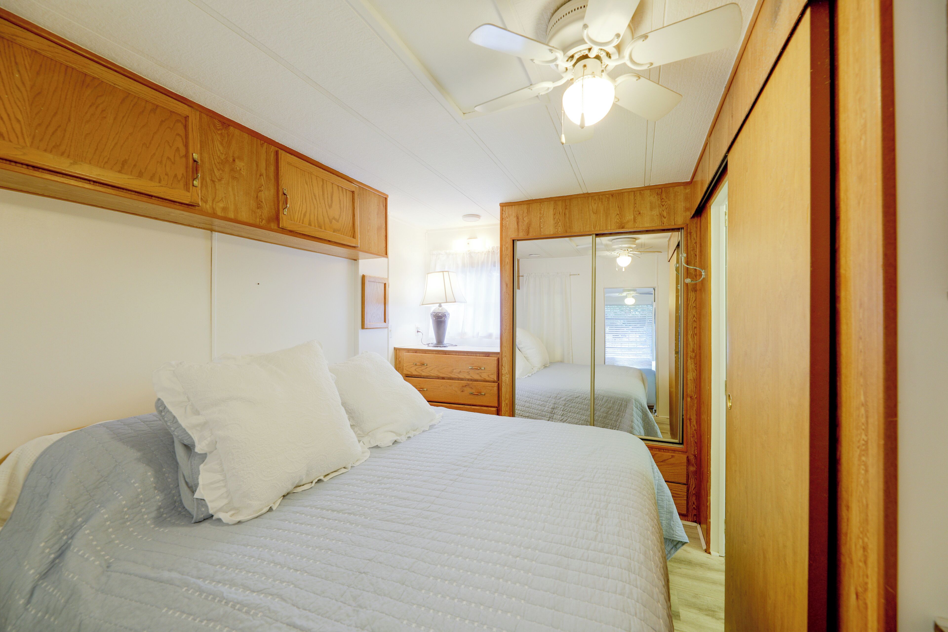 A bedroom with a bed, wooden wardrobe, ceiling fan, and a mirror.