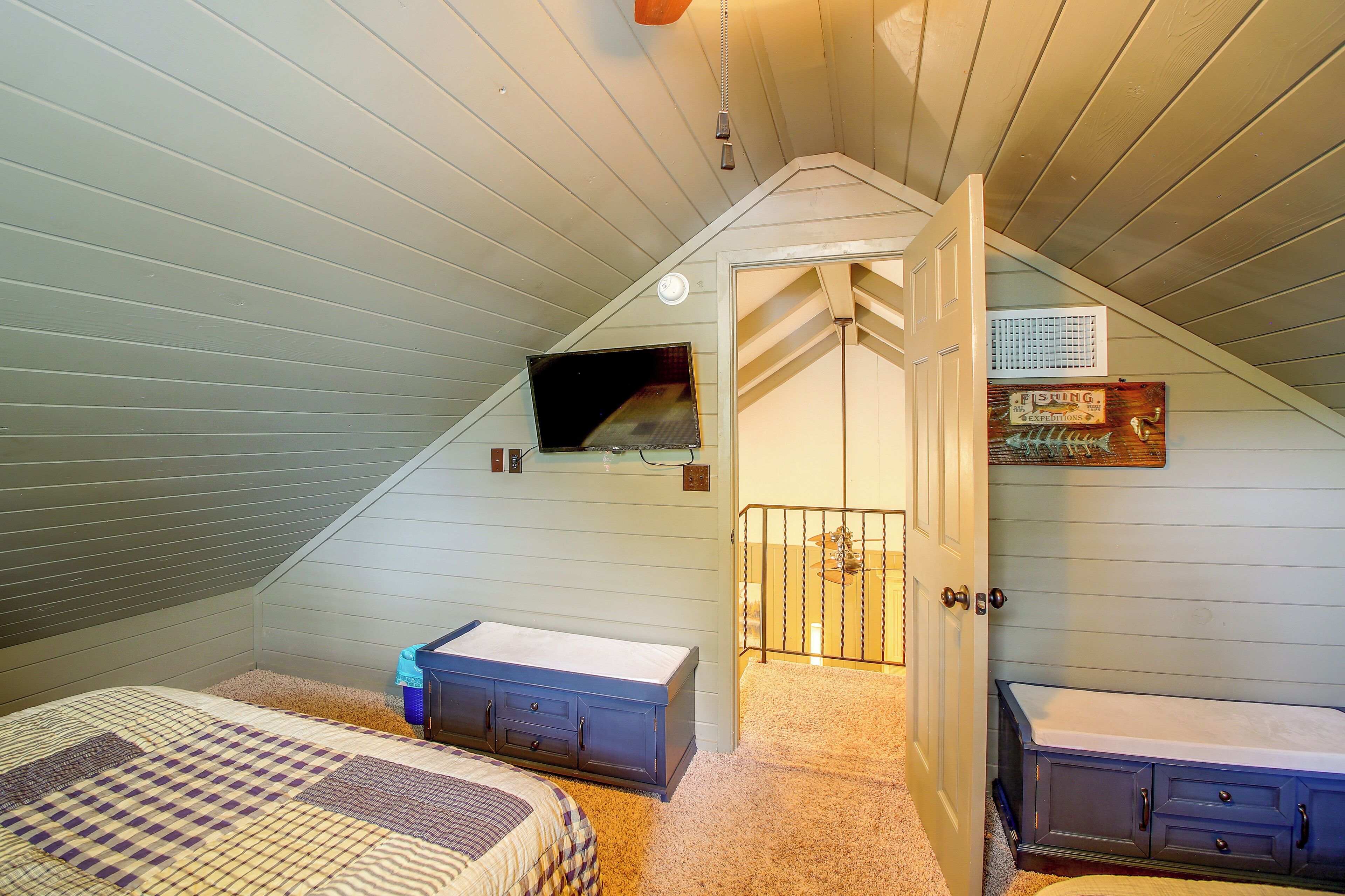 A bedroom with a sloped ceiling, two beds, a dresser, and a small window.