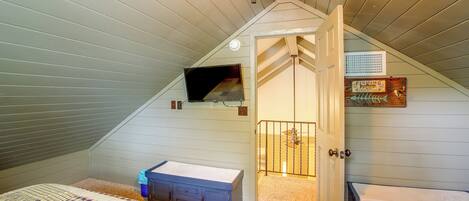 A bedroom with a sloped ceiling, two beds, a dresser, and a small window.