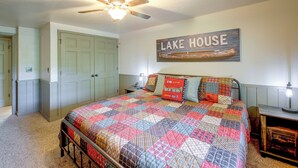 Ein Schlafzimmer mit einem Bett, einem Deckenventilator, einem an der Wand befestigten Schild mit der Aufschrift 'LAKE HOUSE' und einer Tür.