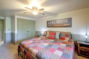 Ein Schlafzimmer mit einem Bett, einem Deckenventilator, einem an der Wand befestigten Schild mit der Aufschrift 'LAKE HOUSE' und einer Tür.