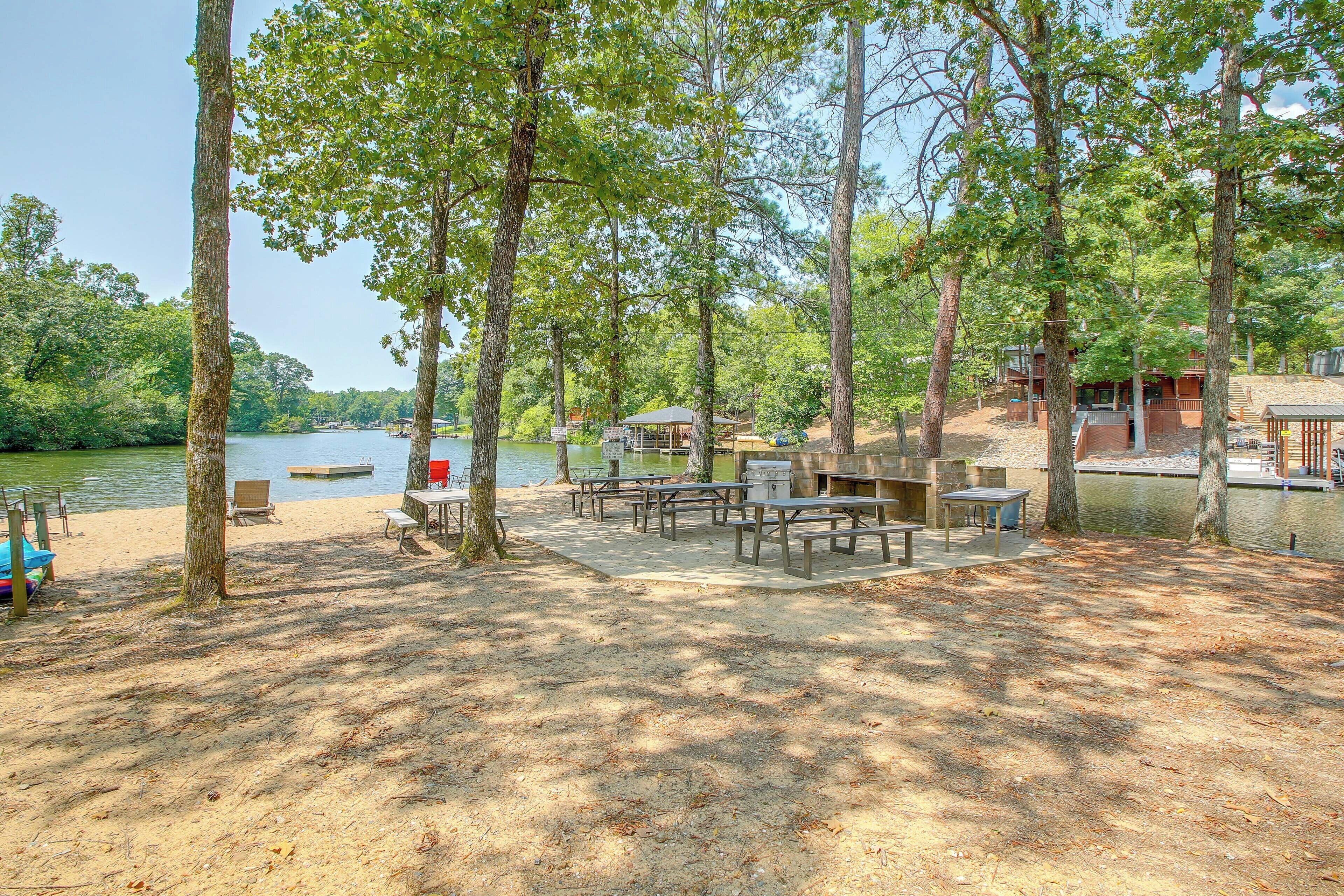 Um camping à beira do lago com mesas de piquenique, área para churrasco e um píer.