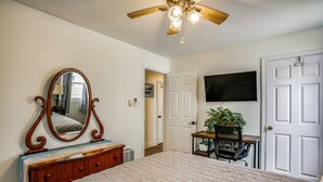 A bedroom with a bed, dresser, mirror, ceiling fan, TV, and a door leading to another room. - Walk to Beach & Marinas! Brigantine 2-unit Duplex (Brigantine)