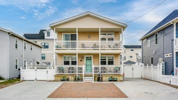 A two-story residential building with a front porch, a gated driveway, and a brick entrance mat.