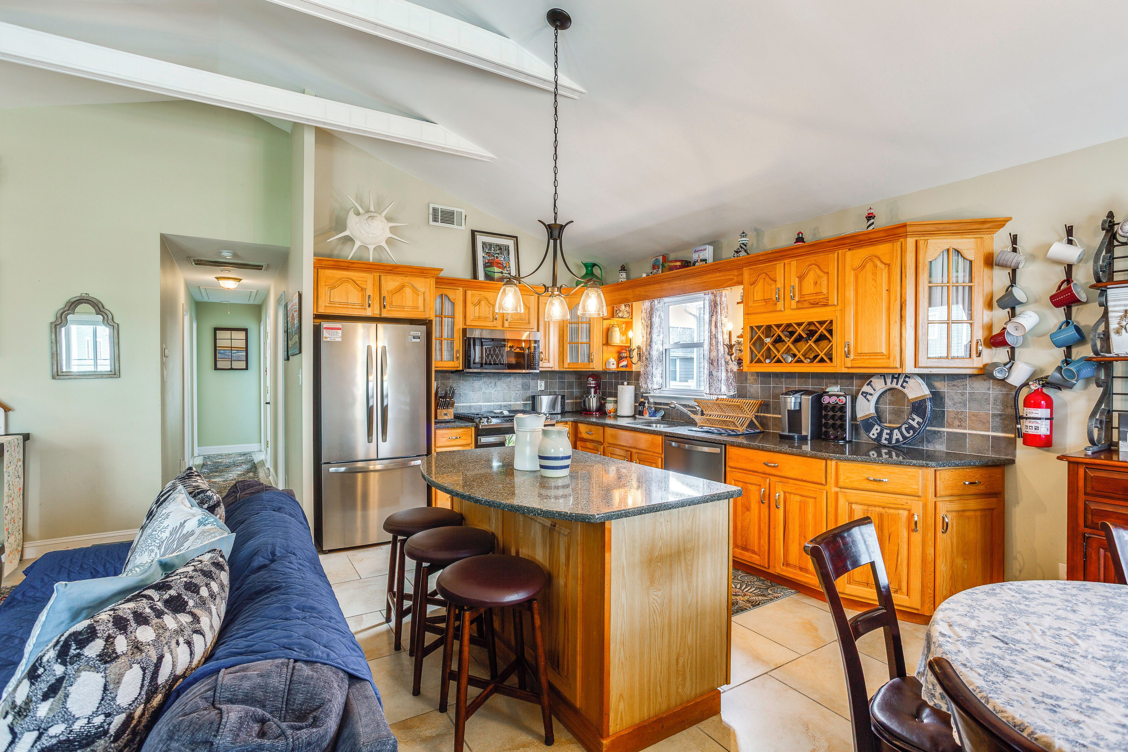 A kitchen with wooden cabinets, a central island, bar stools, a refrigerator, and a dining area with a table and chairs.