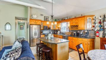 A kitchen with wooden cabinets, a central island, bar stools, a refrigerator, and a dining area with a table and chairs.