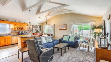 A spacious living area with a sofa, armchairs, and a coffee table. There is a kitchen area with wooden cabinets and a dining table.