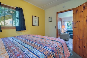 A bedroom with a bed, a window with curtains, a door leading to another room, and a wall-mounted light switch. - Pet-friendly Rustic Cabin Steps From Lake Chetek (Chetek)
