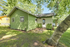A green single-story house with a front porch, a small attached garage, and a yard with grass and trees.