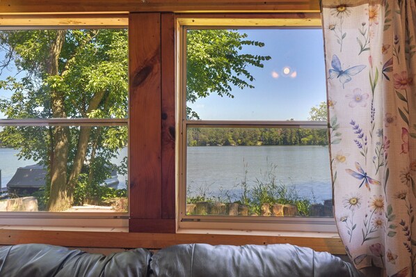 A room with a large window overlooking a lake, a wooden beam structure, and a view of trees and a boat. - Pet-friendly Rustic Cabin Steps From Lake Chetek (Chetek)