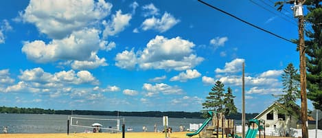A beach with a volleyball net, playground equipment, and a lake in the background.